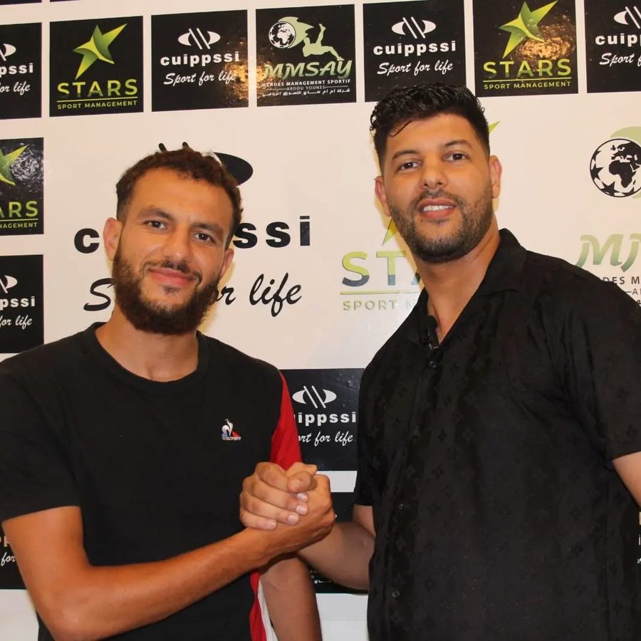Abdou Younes shaking hands with a player in front of the MMSAY backdrop